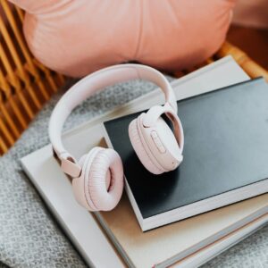 Pink wireless headphones resting on a stack of notebooks with a cozy aesthetic.